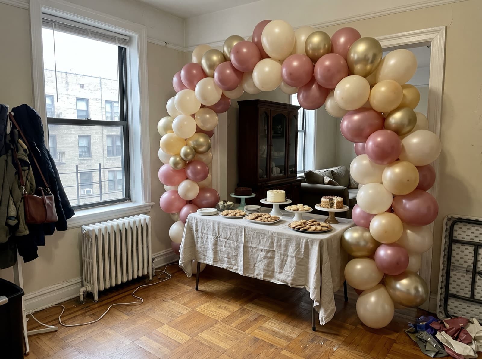 Organic balloon arch in dusty rose, ivory and champagne over a dessert table in a New York apartment