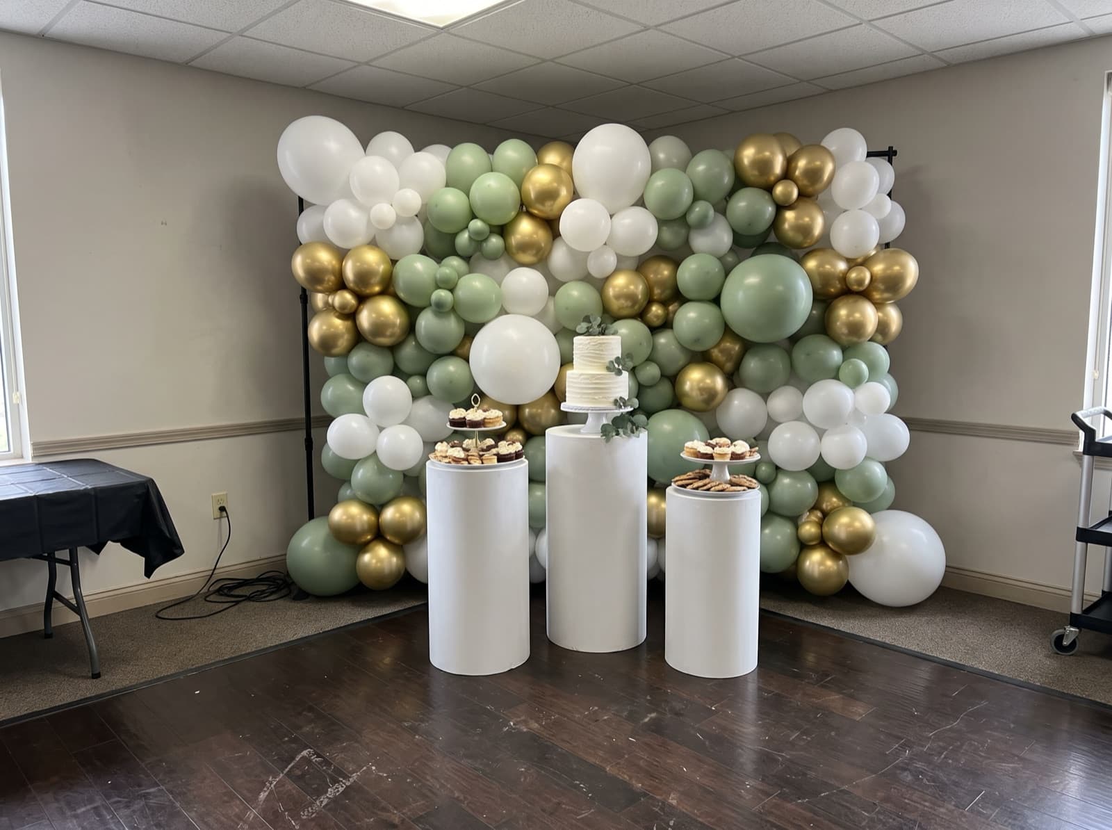 Balloon backdrop with pedestals holding a cake and desserts