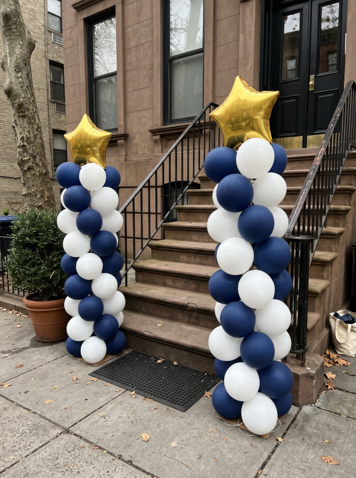 Pair of navy and white spiral balloon columns with gold star toppers at the foot of a brownstone stoop