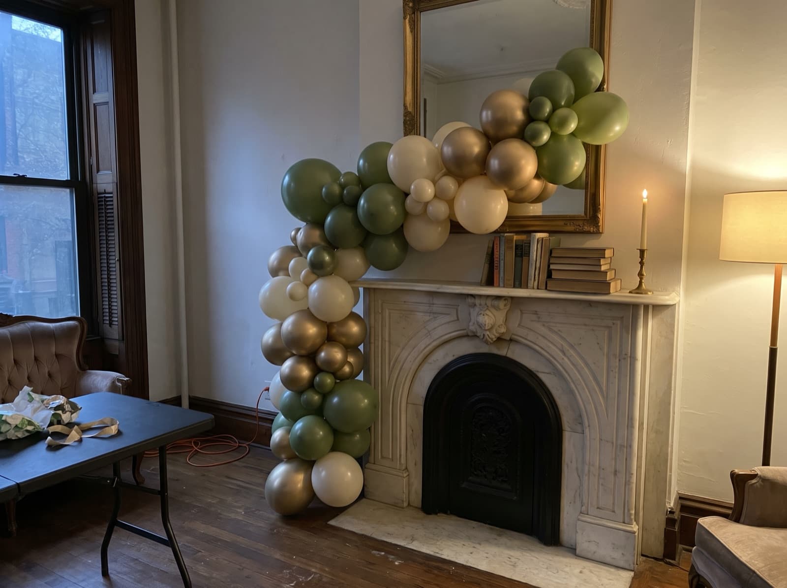 Organic balloon garland in olive, cream and gold draped across a marble mantel in a New York brownstone