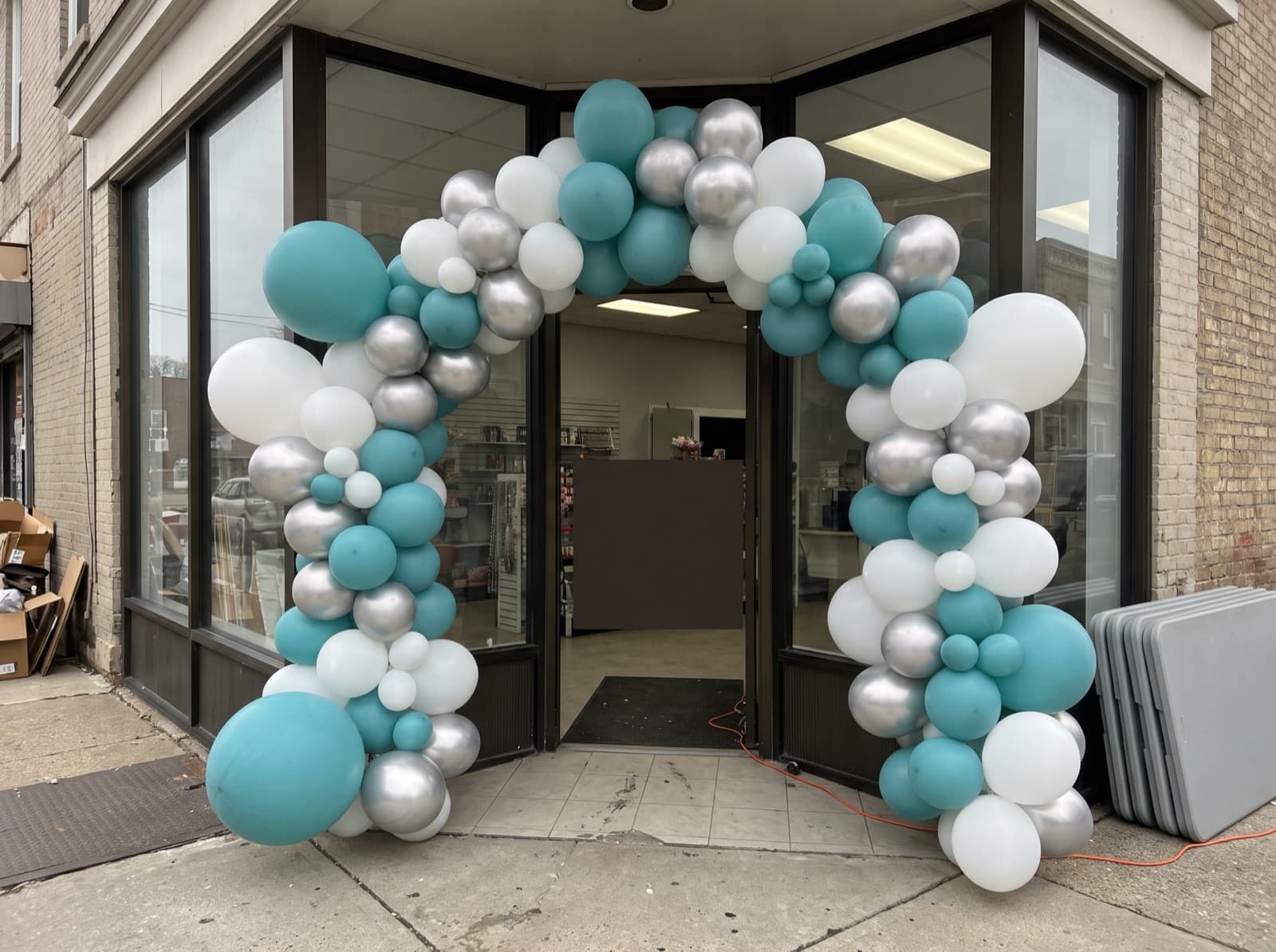 Giant teal, white and silver balloon arch over a corner shop entrance