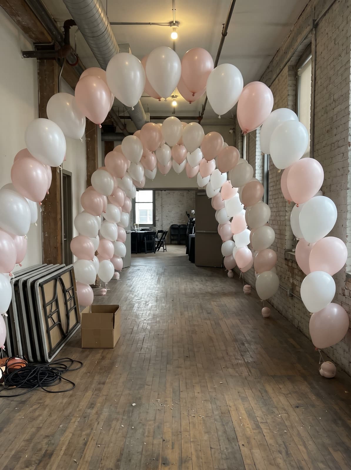 Balloon tunnel of white and blush arches down a loft corridor