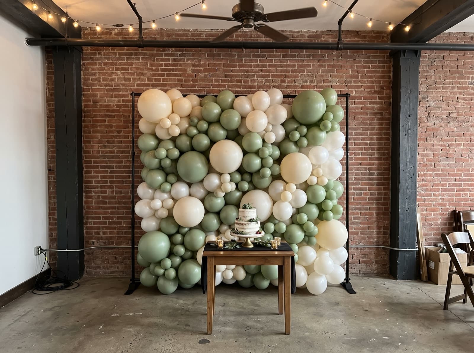Organic balloon wall in ivory, sage and pearl behind a cake table in a New York loft
