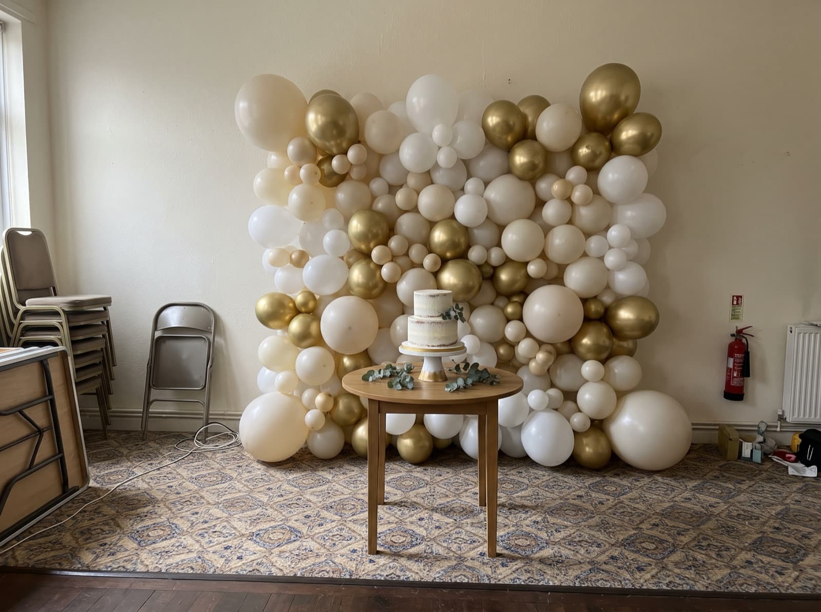 Organic balloon wall in ivory, gold and white behind a cake table